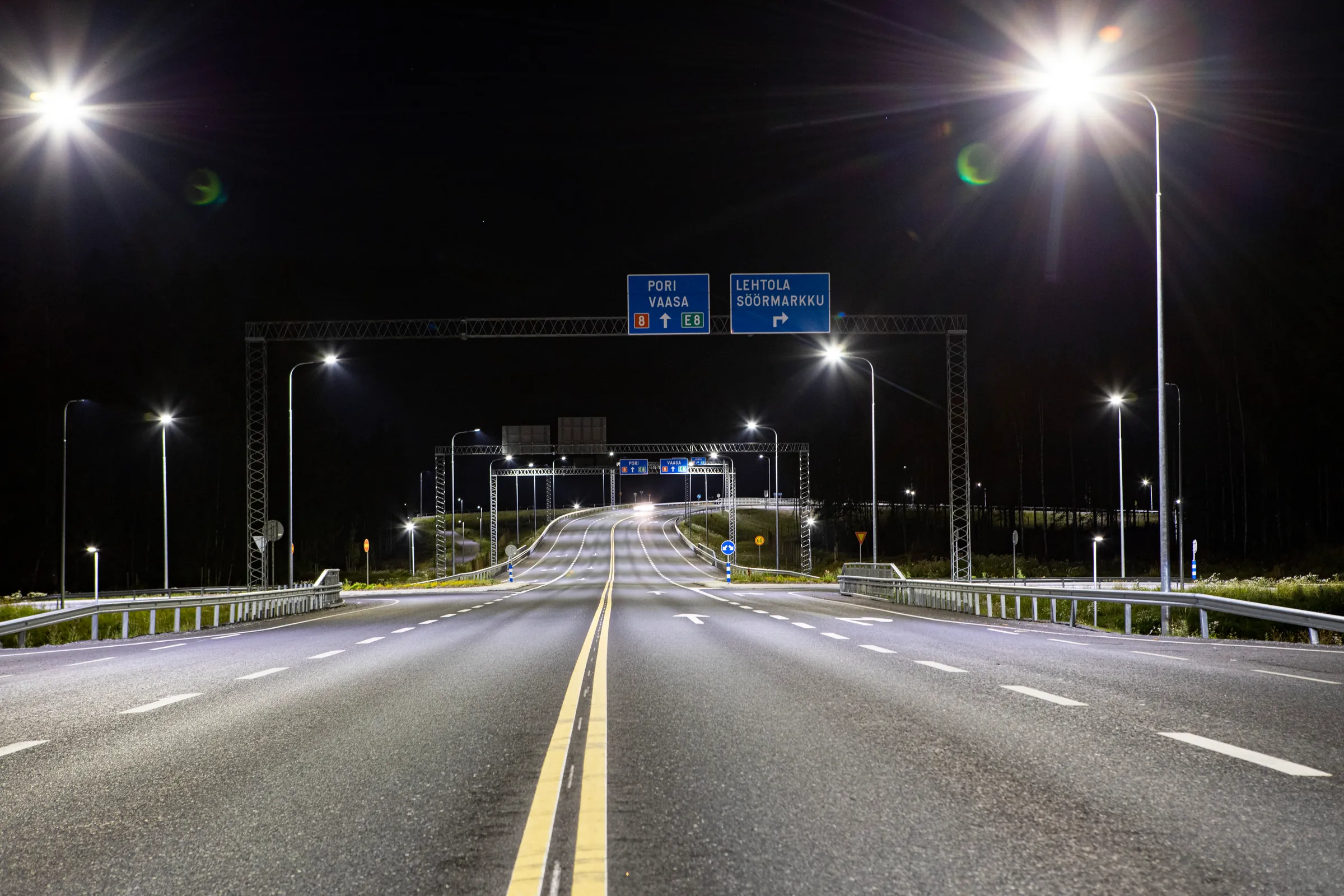 The Söörmarkku junction at night: a KAPU lighting pole stands lit on the right, the road's double yellow centre line runs towards the gantry signs for Pori and Söörmarkku.